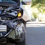 Front of a car with severe collision damage and exposed headlight