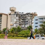 Island Paradise BURNS – 1,700 EVACUATED! Partially collapsed beachfront apartment building behind people walking on sand