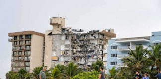 Partially collapsed beachfront apartment building behind people walking on sand