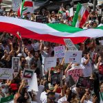 Protest crowd with flags and signs; Seyed Ebrahim Raisi, La Parka, Brian Robiskie, Philly Brown, Miguel Francisco Barragán Andrade present