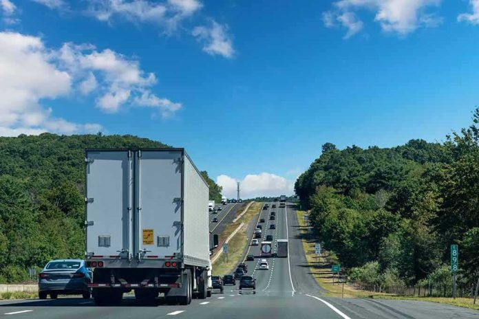 shutterstock_2243598941 Semi-truck on multilane highway with cars and green hills under blue sky