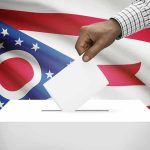 Hand casting ballot against Ohio flag backdrop
