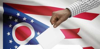 Hand casting ballot against Ohio flag backdrop