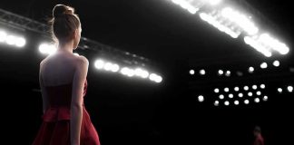 Model in a red dress walking on a runway under bright stage lights