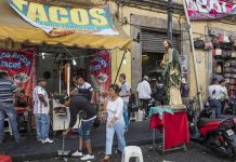 Street taco stand with people and a religious statue on a sidewalk