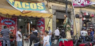 Street taco stand with people and a religious statue on a sidewalk