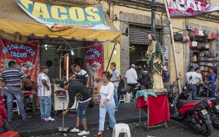 shutterstock_393134476 Street taco stand with people and a religious statue on a sidewalk