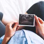 Pregnant Moms Hiding After Latest Trump Announcement Person holding an ultrasound photo over a pregnant belly