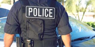 Police officer in tactical vest standing by patrol car