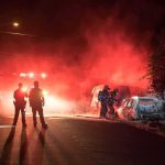 Firefighters and police at a nighttime car fire scene