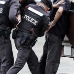 Police officers detain a handcuffed man beside a pickup truck