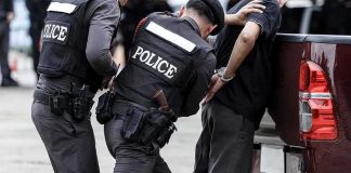 Police officers detain a handcuffed man beside a pickup truck