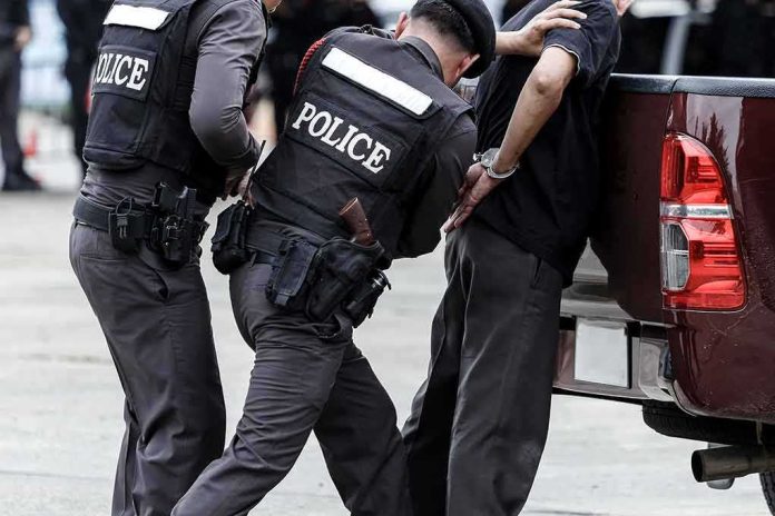 shutterstock_687629158 Police officers detain a handcuffed man beside a pickup truck
