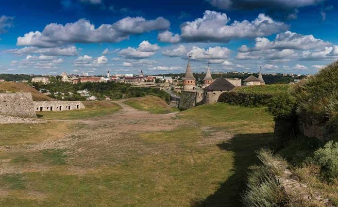 Medieval stone castle with towers on a grassy hill under a cloudy sky