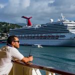 Gay Cruise Denied Entry to Port AGAIN! Man leaning on ship railing looking at a docked cruise ship