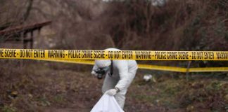 forensic investigator at outdoor crime scene behind caution tape