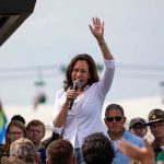 Kamala Harris waves while speaking to a crowd with a microphone