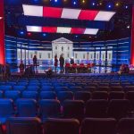 El-Sayed Left Embarrassed After Disastrous Debate Debate stage with red and blue lighting and empty audience seats