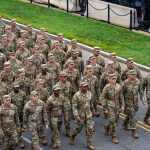 Soldiers in camouflage uniforms march in formation on a street