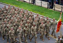 Soldiers in camouflage uniforms march in formation on a street