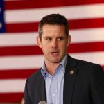 man speaking in front of a large American flag