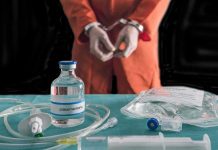 Handcuffed person in orange jumpsuit behind medical vials and IV equipment
